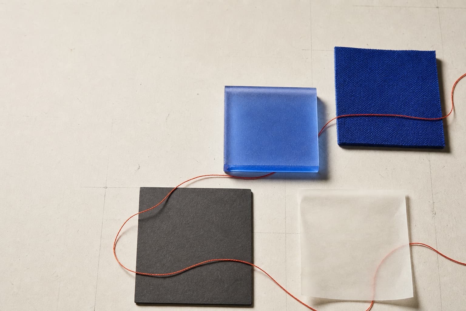 Four tactile material studies connected by a fine coral thread.