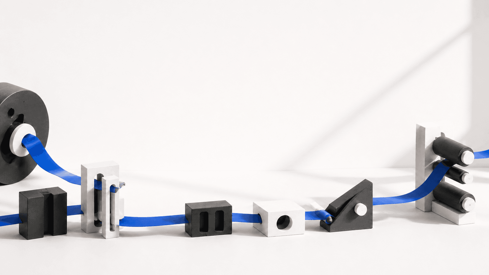 A continuous blue path moving through a series of graphite and metal forms.